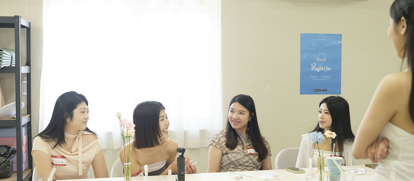 明亮的教室裡,幾位年輕女生坐在鋪著白桌巾的長桌邊聊天試香,桌上擺著香水瓶與插著花的細瓶
