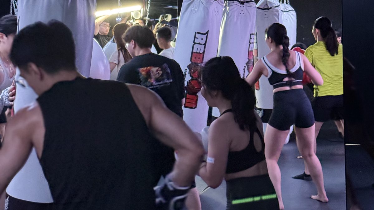 格鬥館裡一整排參加者面向沙包,跟著同一個節奏出拳,畫面多為背影