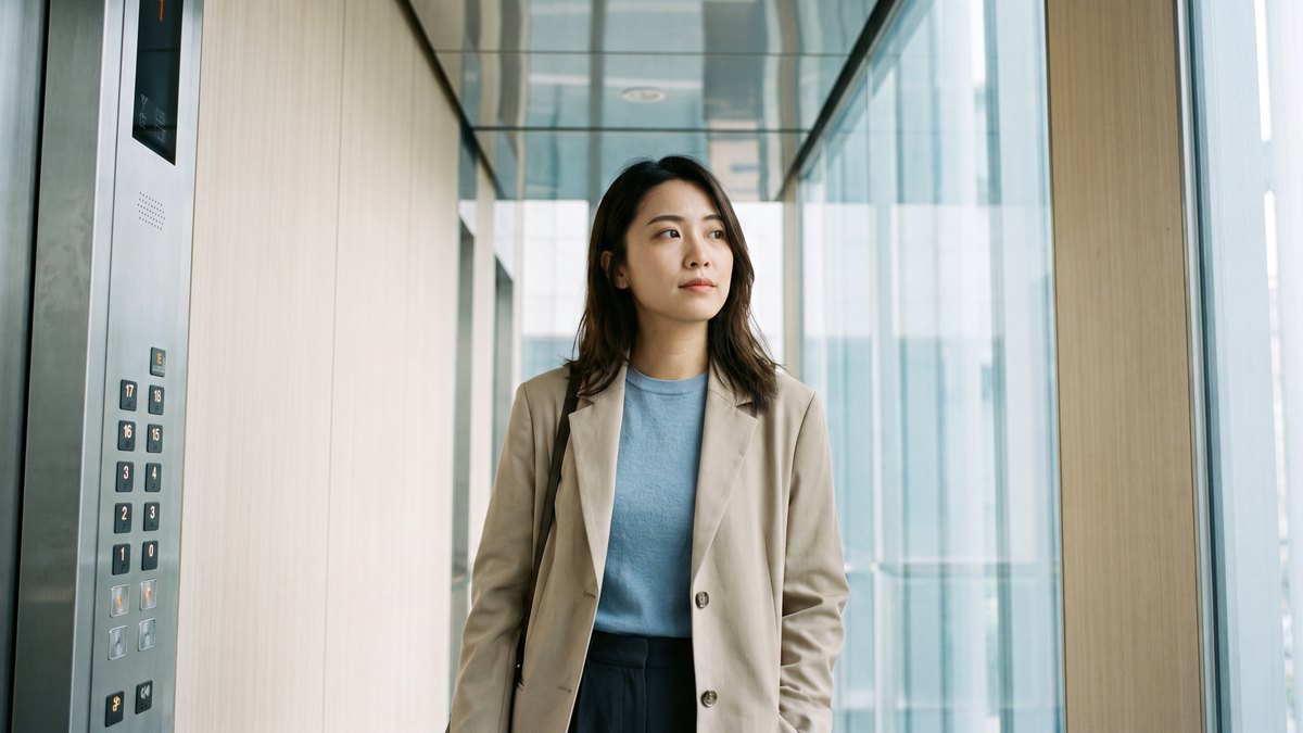 一位女性站在明亮的現代電梯裡，一旁是電梯樓層按鈕面板，若有所思地望向窗外