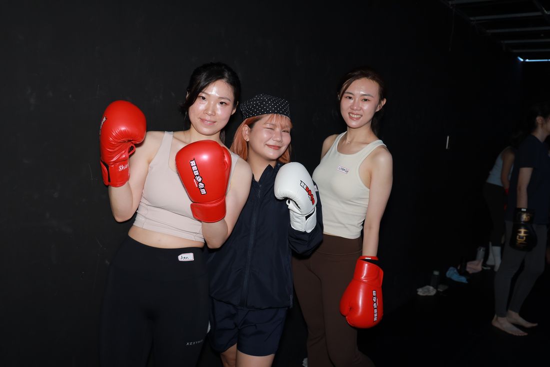 三位女生戴著紅色與白色拳擊手套，靠在一起合照
