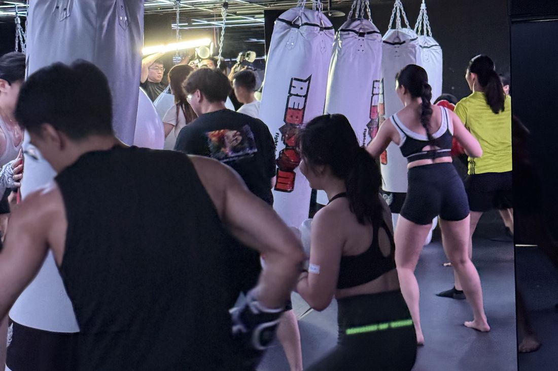 格鬥館裡一整排參加者面向沙包，跟著同一個節奏出拳，畫面多為背影