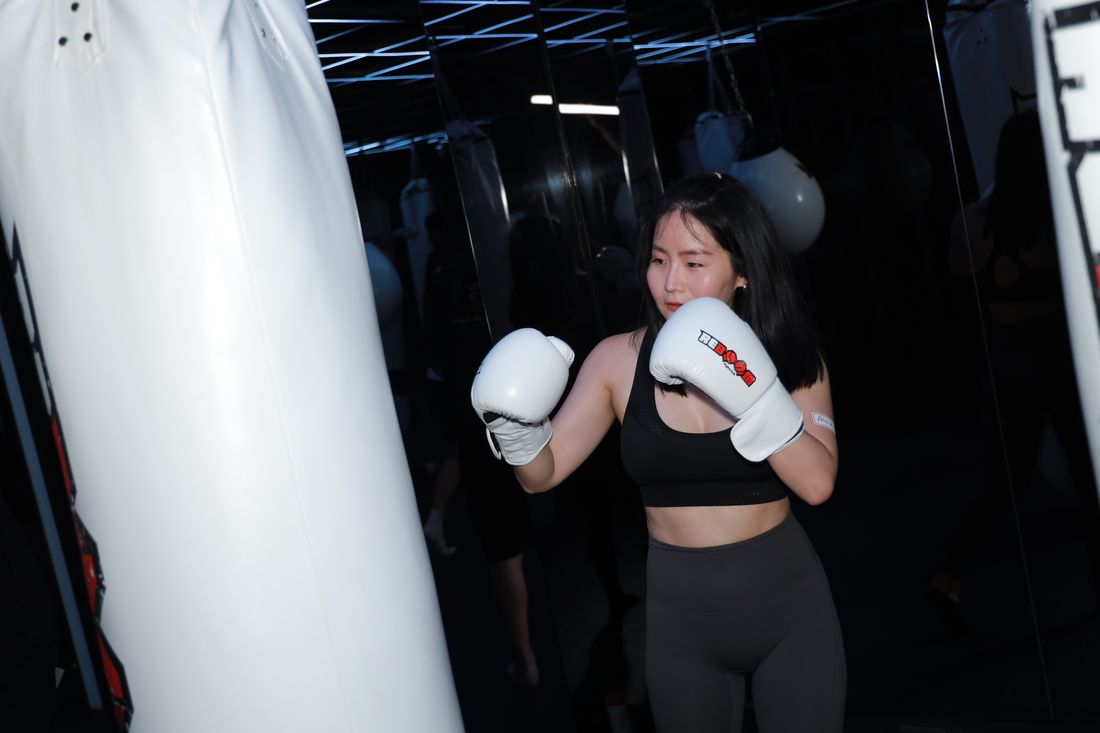 一位女生戴著白色拳擊手套，站在沙包前擺出防守姿勢
