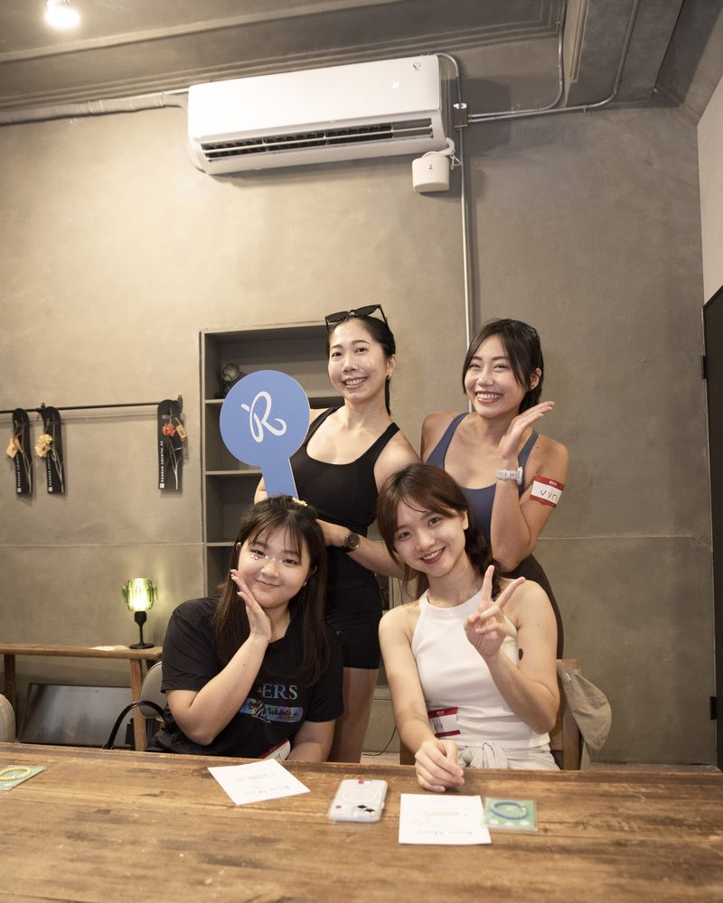 四位女生在報到桌邊比 YA 合照,其中一位舉著藍色的 R 字手拿板