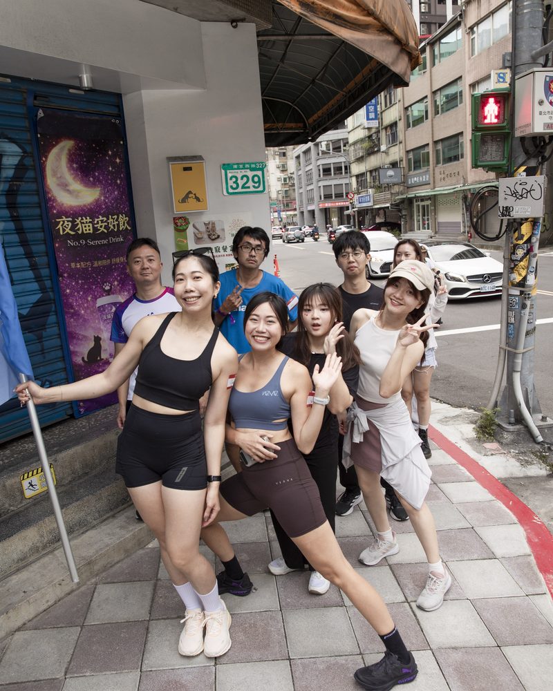 大稻埕街口的騎樓下,一群穿運動服的參加者停下來擺姿勢,最左邊的人扶著藍色旗桿