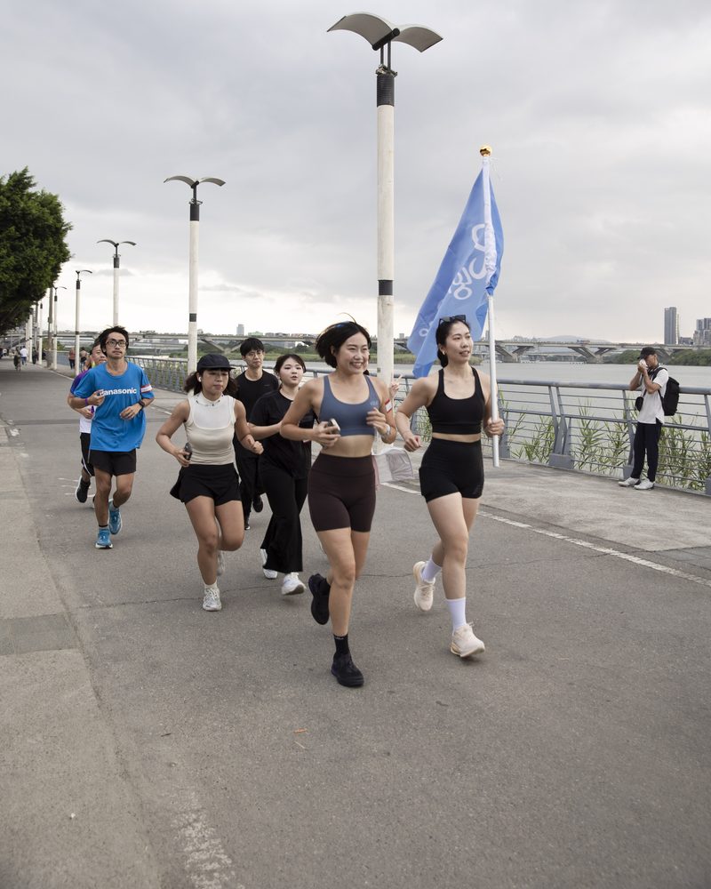 延平河濱的步道上,一群參加者笑著往鏡頭跑過來,後方有人舉著 Right One 藍色旗子
