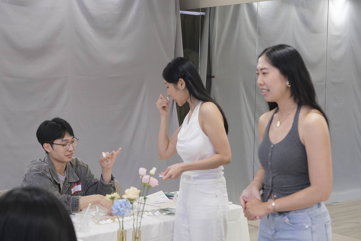 兩位女生站在桌邊聞試香紙,坐著的男生抬頭一起討論