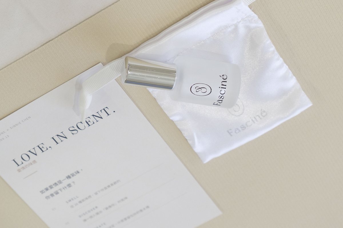 桌上放著印有「LOVE, IN SCENT.」的活動卡,旁邊是一瓶霧面玻璃香水與白色緞面束口袋
